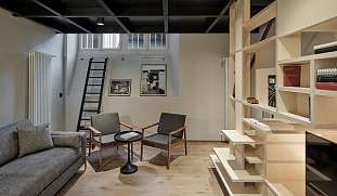 Modern gestalteter Wohnbereich mit grauem Sofa, Designsesseln, Bücherregal und Galerieebene im PARCLOFT Meran I WUNDERORTE