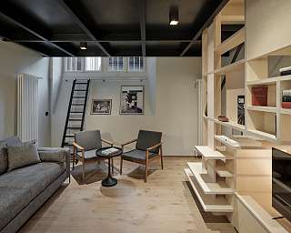 Offener Wohnbereich im PARCLOFT Meran mit minimalistischer Holztreppe, Designregal und Lounge-Sesseln I WUNDERORTE