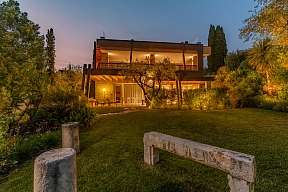 Außenansicht des Lamasu WUNDERORTE Resorts mit moderner Architektur, Zypressen und beleuchtetem Tor bei Dämmerung