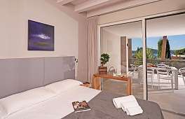 Hell gestaltetes Schlafzimmer der Ferienwohnung Lamasu am Gardasee mit Boxspringbett, Panoramafenster, Seeblick und Zugang zur möblierten Terrasse I WUNDERORTE