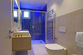 Modernes Wellness-Badezimmer der Lamasu-Ferienwohnung am Gardasee mit Regendusche, blauer Ambientebeleuchtung und Holzwaschtisch I WUNDERORTE