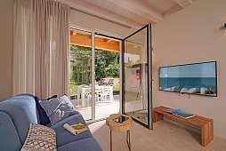 Helles Wohnzimmer der Ferienwohnung Lamasu am Gardasee mit Sofa, TV, Zugang zur Terrasse und Blick ins Grüne I WUNDERORTE