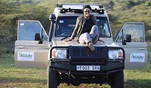 Fransisca sitzt lässig auf einem Safari-Jeep mit dem Logo von Natural Responsible Safari.