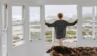 Frau schaut aus geöffnetem Fenster auf das Panorama der Meerklippen
