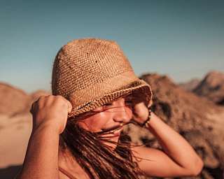 Eine Frau lacht und greift ihren Sonnenhut in der Wüste