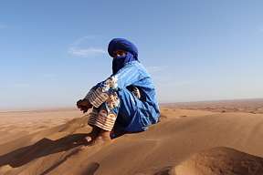 Ein Wüstenguide in traditioneller Kleidung sitzt in der arabischen Wüste – Symbol für Achtsamkeit, Verbundenheit und Kultur bei WUNDERORTE