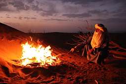 Ein Wüstenbewohner sitzt bei Nacht am Feuer – umgeben von Dunkelheit und Weite. Das Bild fängt die Stille und Würde eines Moments bei WÜSTENFEUER ein, einem der kraftvollsten WUNDERORTE.