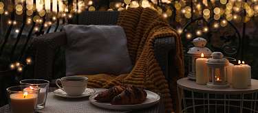 Terrassenambiente in der Herbstzeit mit Kerzenlich und ,Kaffee auf dem Tisch eine  Wolldecke über dem Stuhl symbolisiert Ruhe und Romantik