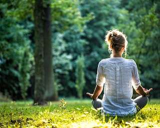 Frau sitzt in Meditationshaltung auf einer sonnendurchfluteten Waldlichtung – Moment tiefer Ruhe, innerer Ausrichtung und bewusster Naturverbindung mit WUNDERORTE.